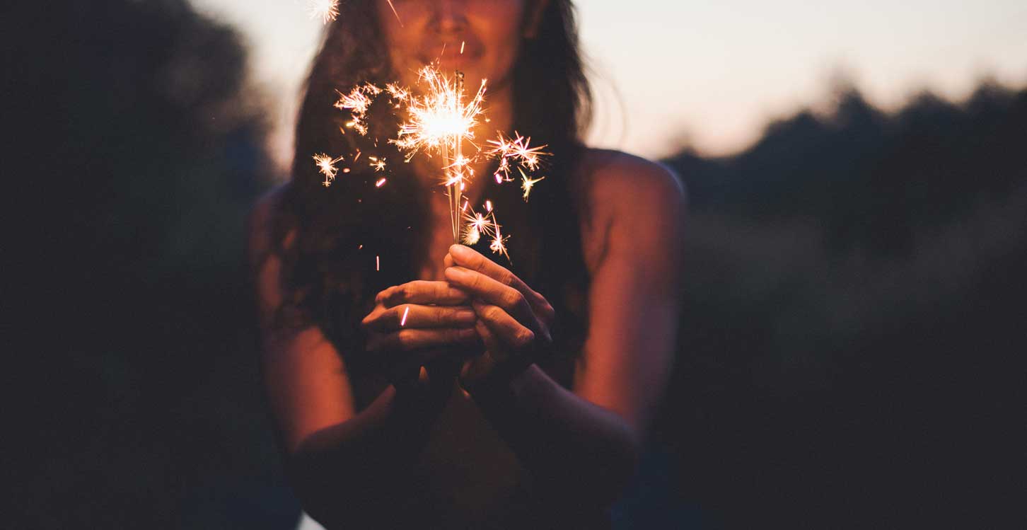 Woman hand holding burning christmas sparkle in twillight sky