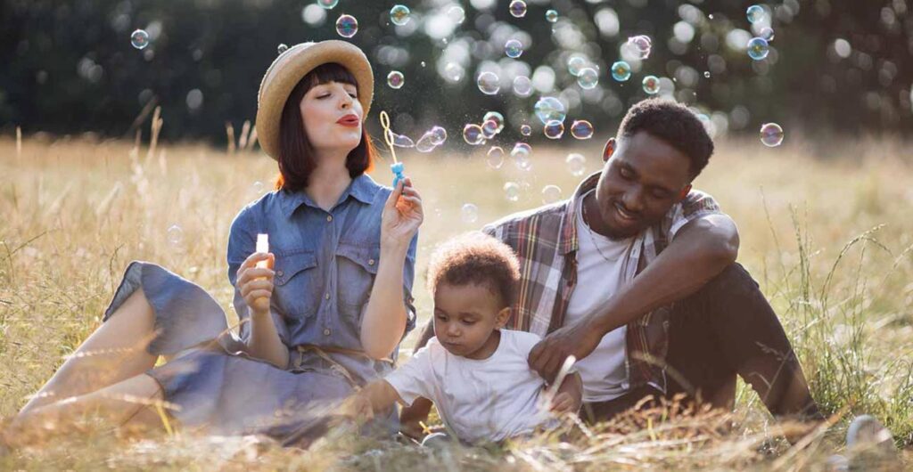 multi ethnic parents with son blowing soap bubbles outdoor